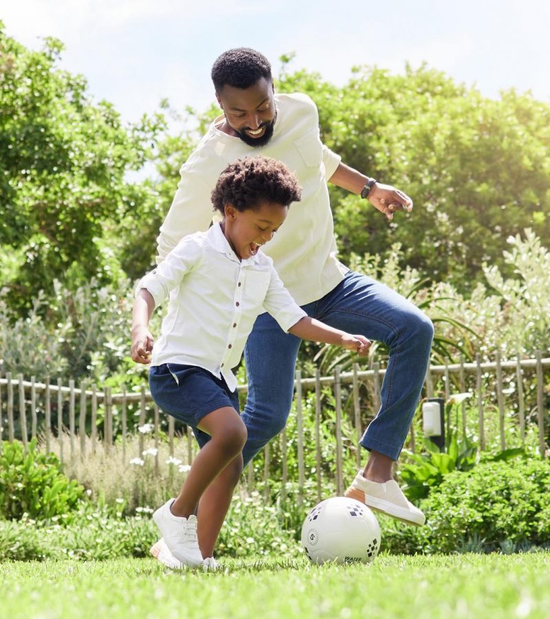 a father and son playing soccer together outdoors.